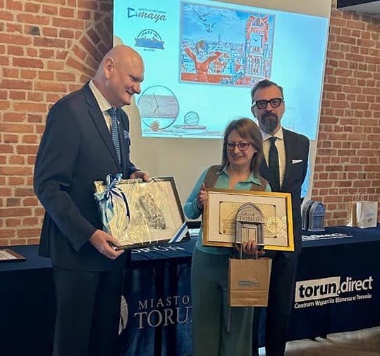 Zdjęcie przedstawia artystkę Maję Wolf odbierającą nagrodę od prezydenta miasta Torunia Michała Zaleskiego. Wręczona nagroda to Made in Toruń