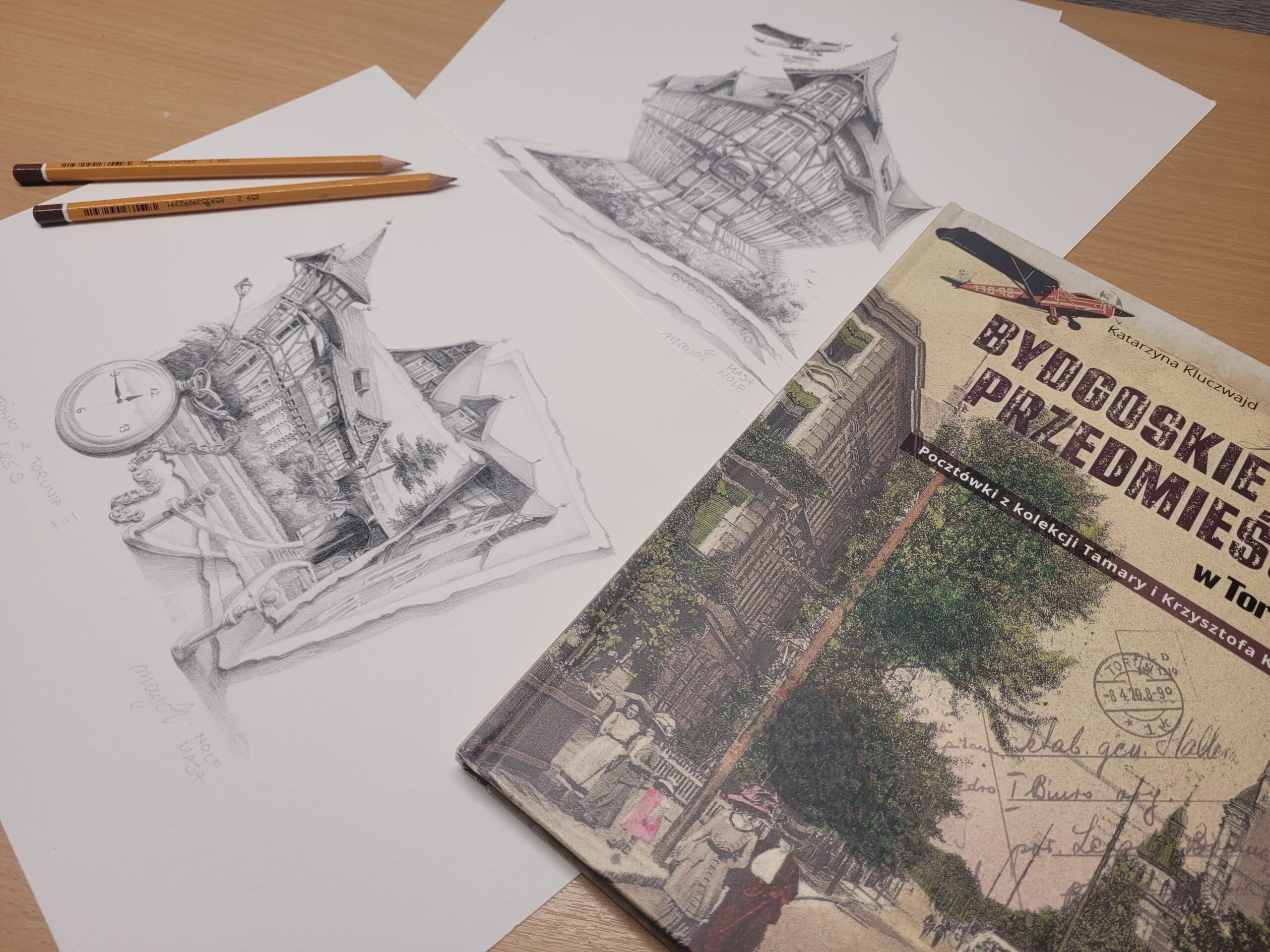 zdjęcie przedstawia album ze starymi zdjęciami "Bydgoskie Przedmieście w Toruniu", 2 rysunki Mai Wolf zainspirowane lekturą tego albumu i 2 ołówki rysunkowe